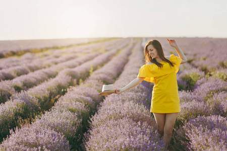 年轻美丽的女人的肖像，穿着黄色的衣服，在紫色的薰衣草花开草地户外，在夏天的自然背景下。 花丛附近的嫩雌性。 生活方式概念