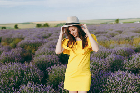 年轻美丽的女人的肖像，穿着黄色的衣服，在紫色的薰衣草花开草地户外，在夏天的自然背景下。 花丛附近的嫩雌性。 生活方式概念