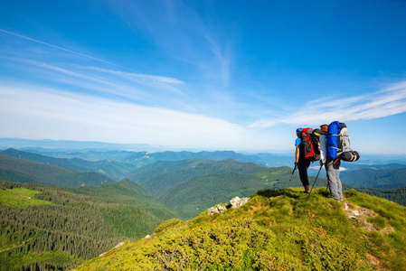 带背包的冒险者站在绿色的山脊上，背景是蓝天，欣赏着群山的全景。 史诗般的旅行在山上。 后视宽角。