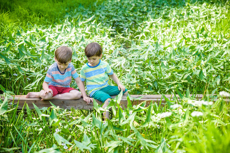 在阳光明媚的夏天或春天，两个小兄弟姐妹可爱的男孩坐在木桥上。 儿童的积极休闲。 小男孩最好的朋友一起在户外玩。