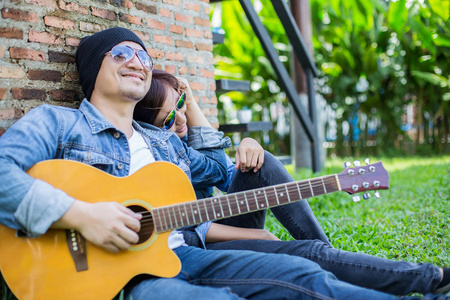 时髦的男人为他的女朋友在户外对着砖墙玩吉他。