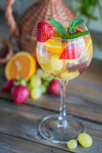 传统夏季饮用白起泡酒桑格里亚。 自制的新鲜水果桑格里亚酒或香槟酒草莓橘子和葡萄，放在带有眼镜和配料的木制乡村餐桌上