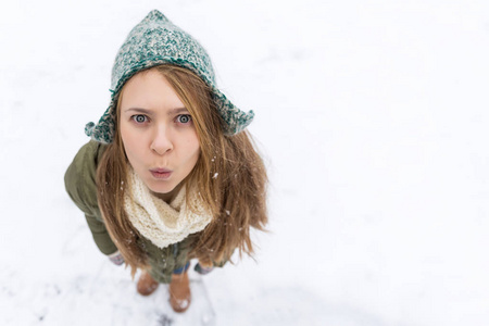 一个金发的年轻漂亮女孩喜欢第一场雪。 绿色夹克，绿色帽子和手套。 上面的风景。 复制空间。