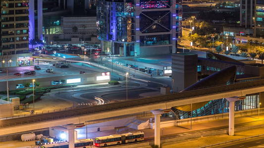 鸟瞰朱美拉湖塔与照明摩天大楼夜间时间推移与汽车停车和交通谢赫扎耶德道路和地铁线。 汽车站靠近地铁站出口。 迪拜码头屋顶景观