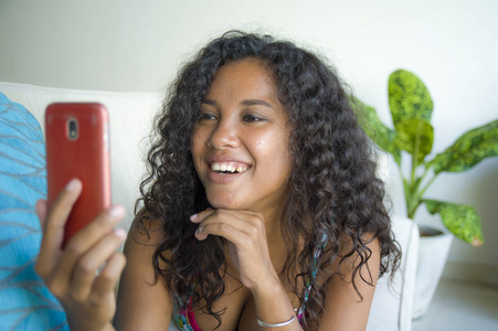 生活方式孤立的肖像年轻快乐和有吸引力的拉丁女人在家里使用手机网络和短信放松在沙发上微笑，快乐享受互联网社交媒体应用程序