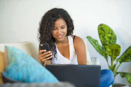 年轻快乐美丽的黑人非裔美国妇女的生活方式肖像，她在家里使用笔记本电脑，沙发沙发，放松