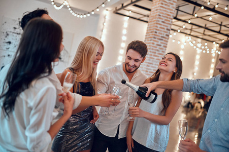 让聚会开始吧 一群年轻人在一起玩得很开心。 在大光灯下的房间里用香槟跳舞。 在亲密朋友的大公司庆祝节日。