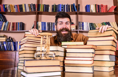 人在快乐的面孔之间的书堆, 而学习在图书馆, 书架上的背景。老师或学生与胡子坐在桌与书, 弥散。馆员理念