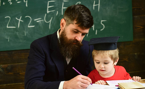 在家上学的概念。老师在正式穿戴和学生在 mortarboard 在教室, 黑板在背景。父亲检查功课, 帮助男孩, 儿子。热心的孩