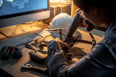亚洲技术工程师使用电动螺丝刀修理无人机与电脑和工具在桌子上。 男性技师修理或维修无人机。 无人机摄影概念
