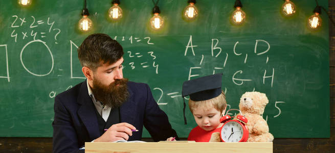 父亲教儿子数学。热心的孩子和老师一起学习。数学课的概念。教师在正式穿戴和学生在 mortarboard 在教室, 黑板在背景上