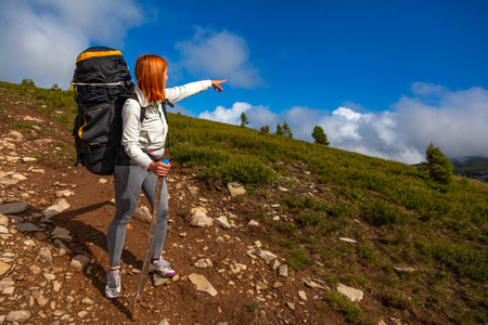 徒步旅行妇女带着背包，享受徒步旅行，并在背景下展示徒步旅行的手方向，一座绿色的田野山。 旅行生活方式和生存概念后景。