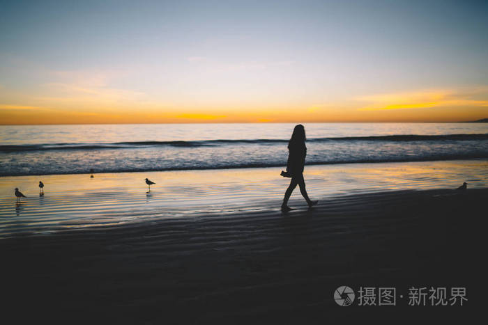 夕阳西下,孤独的女人在宁静的海洋沙岸上剪影,心烦意乱的女孩走在海边