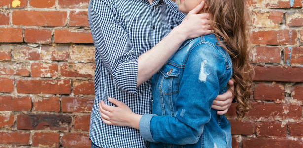 幸福的一对相爱的夫妇拥抱在砖墙背景上的自由空间。 爱的年轻夫妇靠砖墙复制空间