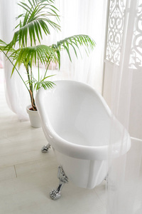 美丽的豪华老式空浴缸靠近大窗户，浴室内部自由空间。 独立的白色浴缸靠近折叠屏和棕榈树复制空间