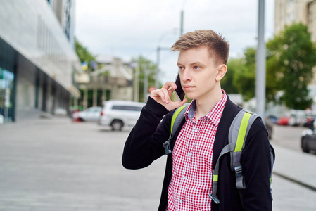 穿格子衬衫的休闲年轻人的肖像，背包在户外漫步，在手机上自由交谈。 旅游和旅游概念