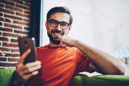 成功留胡子的男性博主在智能手机设备上通过免费4G互联网连接下载应用程序时嘲笑相机的肖像。积极的嬉皮士在网上付款