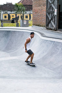 一个穿着白色T恤和帽子的时髦年轻人在游泳池里溜冰的溜冰场上玩滑板。
