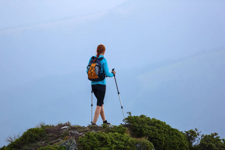 那个带着旅游设备的女孩带着草坪登上了岩石高地的顶峰。雾中的山景..