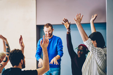 快乐的多元文化团队年轻人穿着智能休闲服，举起双手，庆祝成功的创业项目和在现代办公室室内比赛中的胜利