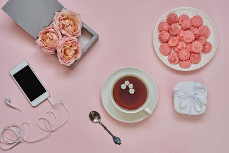 工作空间与智能手机，一杯热凉茶花和棉花糖在粉红色的桌子上。 女性办公桌的创造力。 仍然生活的粉红色项目与粘贴口音。 上面的风景。