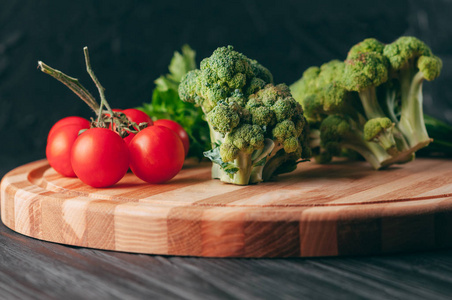 在一张深色的木桌上，在一块圆木板上，新鲜的绿色西兰花欧芹和樱桃番茄，为您的健康服务。 食谱。 配料。 饮食食物。 放在课文下面