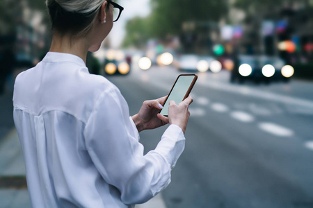 年轻女性手里拿着现代智能手机，在网上聊天中留言，站在城市街头。女性博客作者在手机上发送短信，屏幕空白