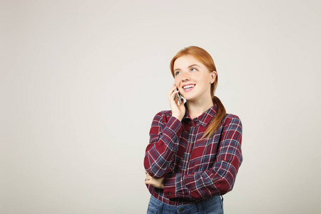 年轻漂亮女人的肖像，留着红色长发，穿着法兰绒衬衫，在手机上聊天。 微笑迷人的女性有智能手机交谈。 隔离背景拷贝空间关闭