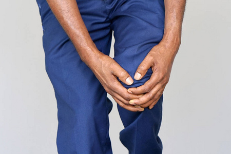 膝盖疼。 关闭非洲男性腿与痛苦的膝盖在灰色背景。 男人感到关节疼痛，有健康问题，用手摸腿。 身体和保健概念。