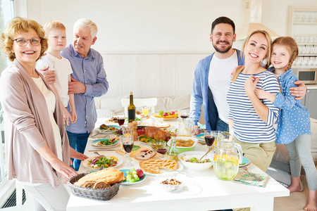 在现代阳光公寓复印空间，幸福的两代家庭在节日中，他们在节日庆祝期间，摆着美味的菜肴和微笑的圆桌，享受晚餐