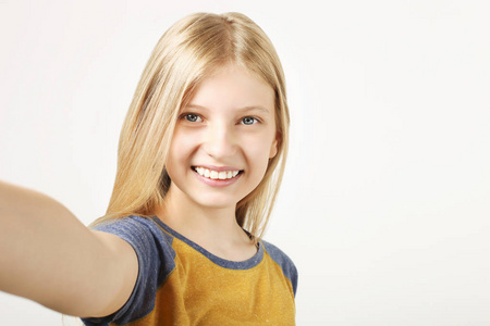 年轻美丽的少女的肖像，完美的微笑，笑着手里拿着手机。 快乐的年轻女子自拍与她的智能手机隔离在白色背景。 复制空间。