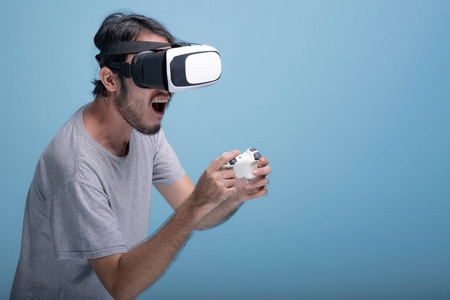 年轻的胡须男在蓝色背景下玩虚拟现实游戏。 非常专注的亚洲年轻人穿着VR耳机半身体射击。 年轻一代的嬉皮士放松概念。
