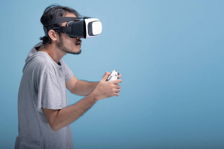 年轻的胡须男在蓝色背景下玩虚拟现实游戏。 亚洲年轻人戴着VR耳机半身射击。 年轻一代的嬉皮士放松概念。
