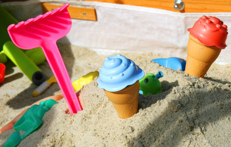 阳光下沙子里五颜六色的玩具。 带有一些阴影的木制沙箱。