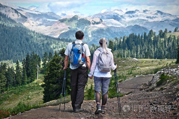 已婚夫妇带着背包和徒步旅行杆在山上散步.