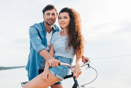 幸福的年轻夫妇坐在海边的自行车上