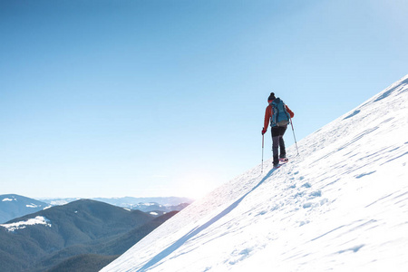 一个人爬到山顶。 穿雪鞋的登山者背着一个背包。 冬天在山上旅行。 大自然中的极端假期。 极端条件下的游客。