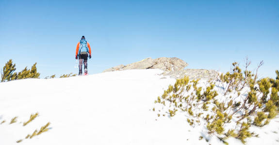 一个人爬到山顶。 穿雪鞋的登山者背着一个背包。 冬天在山上旅行。 大自然中的极端假期。 极端条件下的游客。