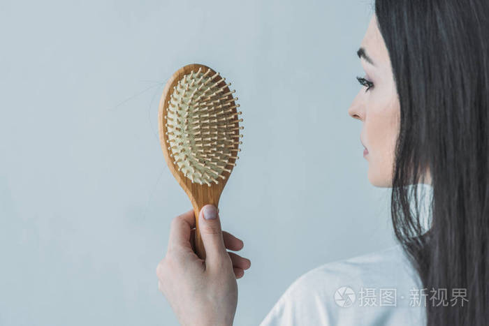 一个黑发女人拿着梳子,头发落在灰色上