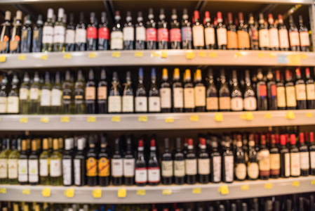 模糊的图像的葡萄酒货架与价格标签显示在休斯顿得克萨斯州美国商店。 分散了超市货架上的一排排酒酒瓶。 酒精饮料抽象背景。