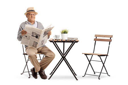 老人坐在咖啡桌旁，手里拿着一张孤立在白色背景上的报纸