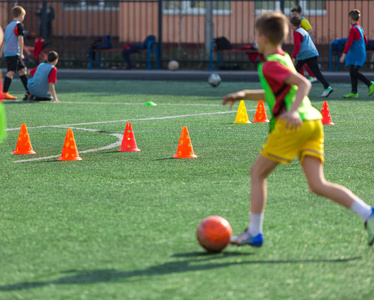 可爱的男孩踢足球快乐的孩子享受足球。 孩子们活动小足球运动员。 夏季野外训练