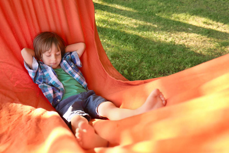 阳光明媚的一天，可爱的小男孩在户外吊床上放松