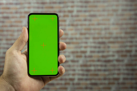 一个男人的手拿着一个全屏手机在砖墙前。 视频复制空间的绿色屏幕。