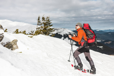 冬天爬山。 一个穿雪鞋的人正在爬到山顶。 冬天上升。 一个带背包和徒步旅行棒的登山者。 冬季徒步旅行的设备。