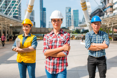 三名工业工程师戴安全帽工程站在外面的建筑上，手臂交叉。 工程工具和施工理念。
