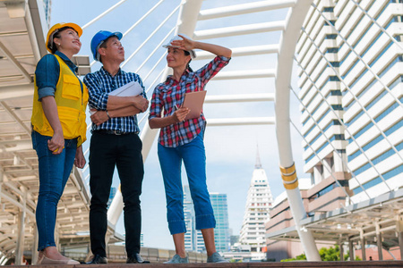 三名工业工程师戴安全帽，手持平板工程，在建筑外进行图纸检查。 工程工具和施工理念。 副本空间
