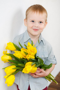 微笑的男孩手拿一束黄色郁金香站在白墙旁的画像