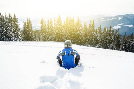 一个穿着蓝色滑雪服的人正坐在山顶上的雪地上