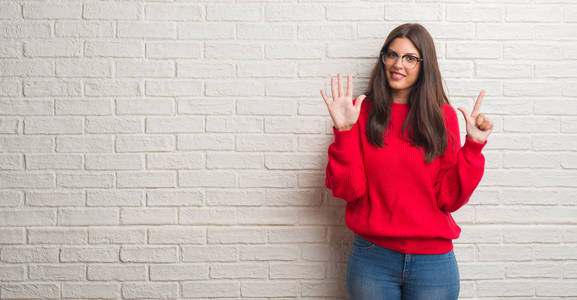年轻的黑发女人站在白色砖墙上，用手指举着七号，微笑着自信和快乐。
